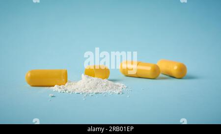 scatter powder from yellow gelatin capsule pills, open oral medical drug filled with powder on blue background, side view with copy space, taken in se Stock Photo