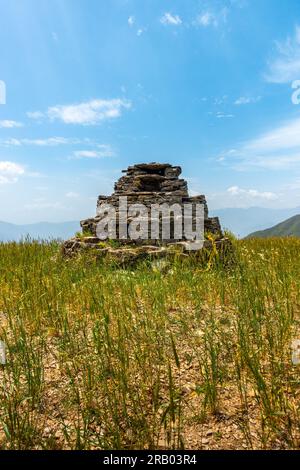 An ancient small pyramid shaped worship idol prayer place made of stones in the middle of a meadow with beautiful landscapes. Cultures of The Himalaya Stock Photo