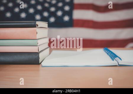 A simple composition of many books, stack or pile of books on wooden table with United States of America flag. One of them open with copy space. Stock Photo