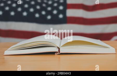 A simple composition of many books, stack or pile of books on wooden table with United States of America flag. One of them open with copy space. Stock Photo