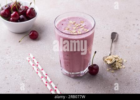 Milkshake with cherries, yogurt and oatmeal, drinking straws, bowl with fresh cherries on a beige textured background Stock Photo