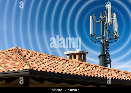 Closeup of a house roof with a telecommunications tower with antennas (aerial) and radio waves, against a clear blue sky with clouds and copy space. Stock Photo