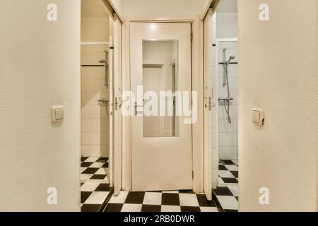 a bathroom with black and white checkered tiles on the floor, and an open door leading to a walk - in shower Stock Photo