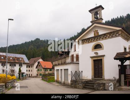 A residential road in the village of Ovaro, Carnia, Udine Province, Friuli-Venezia Giulia, north east Italy. Oratorio di Santa Teresa Church on right Stock Photo