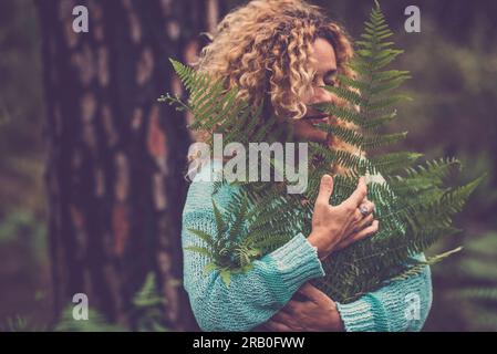 One woman hugging big tropical leaves. Nature lover and environment lifestyle. People feeilng and connection with nature. Happiness life. Forest green woods ambient protection concept image. Balance Stock Photo