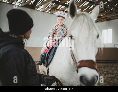 Mother and daughter with horse in riding hall Stock Photo