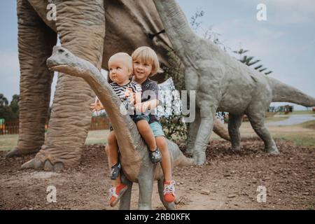 Brother and sister sitting on dinosaur sculpture Stock Photo