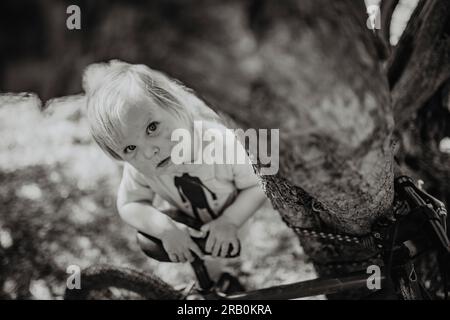 Little girl with bicycle leaning against tree Stock Photo