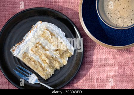 A single plated serving of a home made lemon meringue cake served to a table plated. the cake has a lemon curd filling and buttercream frosting Stock Photo