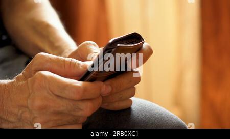 An elderly man's hands, covered with knotted veins, search for coins in his wallet Stock Photo