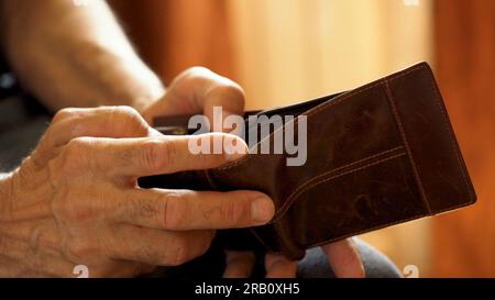 An elderly man's hands, covered with knotted veins, search for coins in his wallet Stock Photo