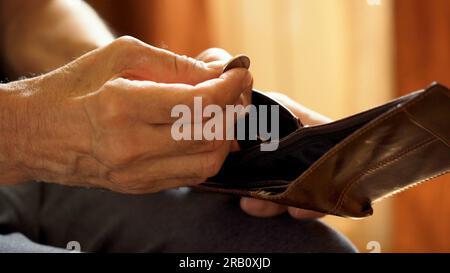 An elderly man's hands, covered with knotted veins, search for coins in his wallet Stock Photo