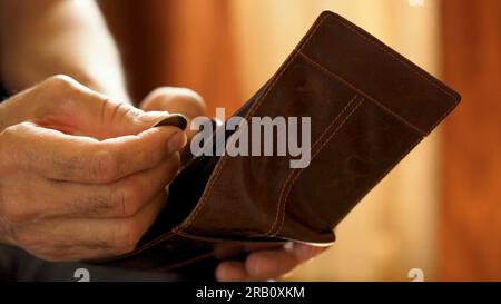 An elderly man's hands, covered with knotted veins, search for coins in his wallet Stock Photo