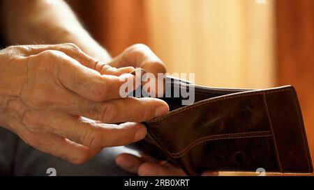 An elderly man's hands, covered with knotted veins, search for coins in his wallet Stock Photo