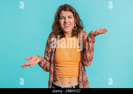 What Why. Sincere irritated young woman raising hands in indignant expression, ask reason of failure demonstrating disbelief irritation by trouble. Pretty confused brunette girl on blue background Stock Photo