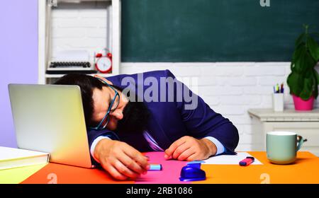 Tired overworked teacher sleep at desk. Knowledge, education and learning concept. Sleeping male student in classroom. Bearded man in glasses sleep in Stock Photo