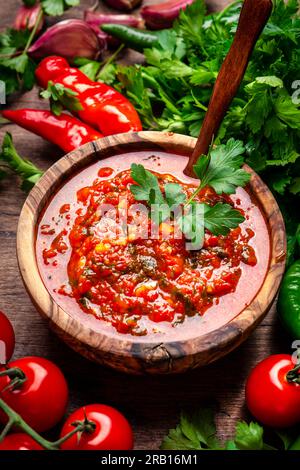 Traditional armenian spicy adjika sauce with hot pepper, paprika, tomatoes, garlic and parsley on rustic wooden kitchen table background, top view Stock Photo