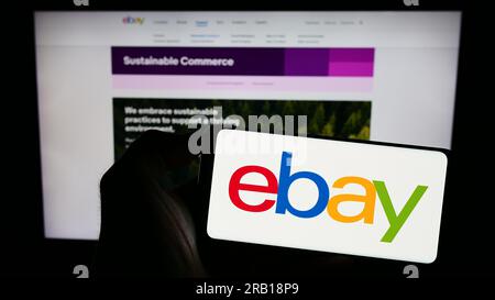 Person holding cellphone with logo of US e-commerce company eBay Inc. on screen in front of business webpage. Focus on phone display. Stock Photo