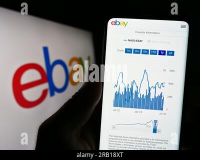 Person holding cellphone with website of US e-commerce company eBay Inc. on screen in front of business logo. Focus on center of phone display. Stock Photo