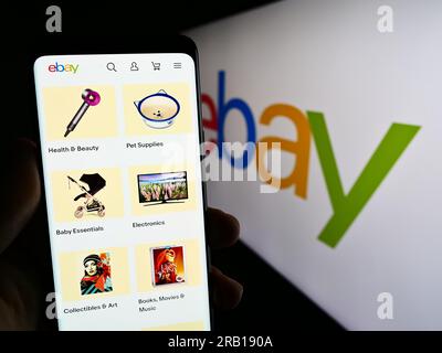 Person holding smartphone with web page of US e-commerce company eBay Inc. on screen in front of business logo. Focus on center of phone display. Stock Photo