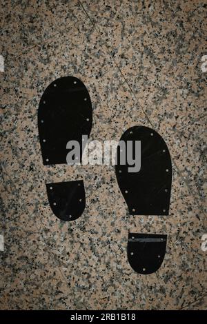 Two black footprints of male shoes on tile floor Stock Photo
