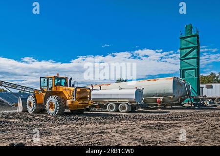 A boxy green tower stands in a flattened area in an active landfill, with vehicles nearby. Stock Photo