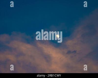 Moon in a blue sky with pink sunset lit clouds Stock Photo