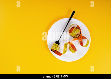 Diet, Weight Loss Concept, Empty Plate with Measuring Tape and Fork Over Yellow Background Stock Photo