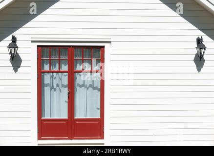 Red framed glass door of small wooden shed with empty wall of white painted horizontal boards Stock Photo