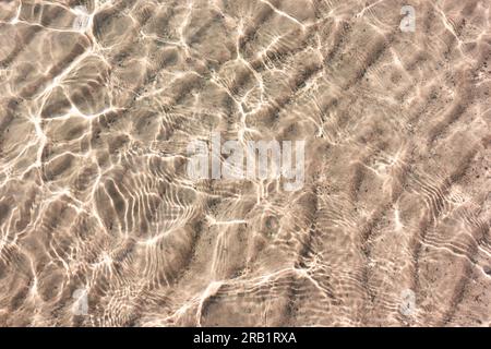 White sand pattern under clear transparent water with reflection of the sun in small waves from paradise beach Stock Photo