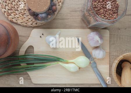 Background for a book with a still life composition with green onions, garlic, spices and kitchen utensils on a wooden background. Stock Photo
