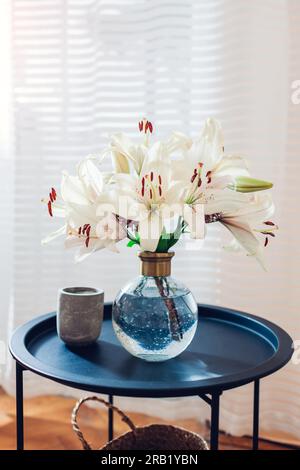 Close up of summer bouquet of roses flowers put in transparent vase on table by window. Cozy interior and decor at home. Space Stock Photo