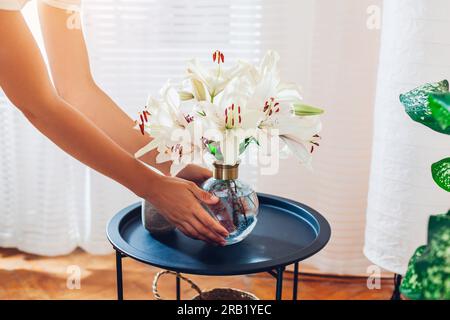 Woman puts transparent vase with bouquet of roses flowers on table. Taking care of interior and summer decor at home. Close up Stock Photo