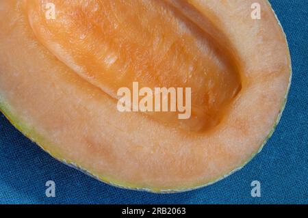 A close-up photo of a fresh and enticing cantaloupe melon, accentuated by a dark blue woven cloth backdrop. The top view captures its refreshing appea Stock Photo