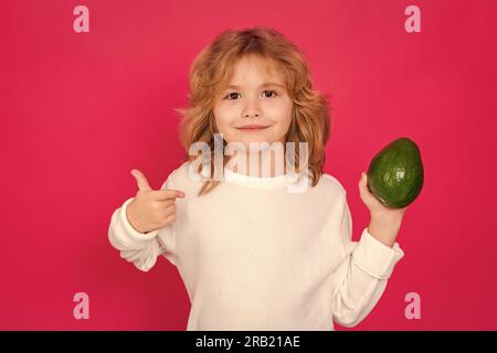 Kid hold red avocado in studio. Studio portrait of cute child with avocado isolated on red background Stock Photo