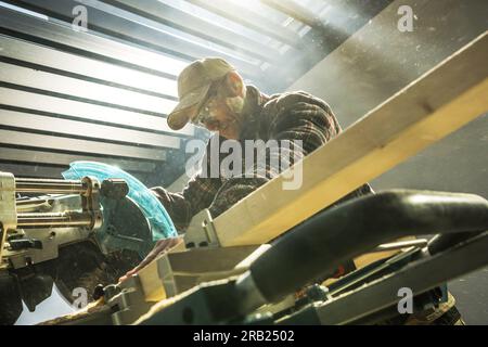 Professional Caucasian Woodworker Cutting Wooden Plank with Table Saw in His Woodworking Workshop. Construction Theme. Stock Photo
