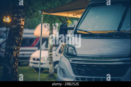 Closeup of Modern White Camper Van with Rolled Out Awning Parked at RV Campground for Overnight Stay. Camping and Motorhome Traveling Theme. Stock Photo