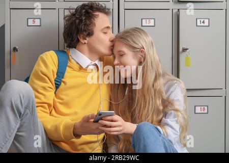 Cute teenage couple with earphones listening to music near locker at school Stock Photo