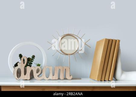 Small mirror, books and florarium on white table near grey wall, closeup Stock Photo