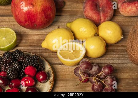 Ripe cherries, seedless grapes, lemons and limes and berries on an unvarnished wooden table Stock Photo