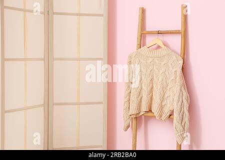 Sweater hanging on wooden ladder and folding screen near pink wall in room Stock Photo