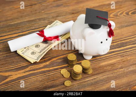 Stacks of coins, piggy bank in graduation cap, dollar banknotes and diploma on wooden background. Student loan concept Stock Photo