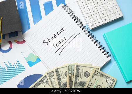 Notebook with text STUDENT LOANS, calculator, graduation cap, charts and dollar banknotes on blue background Stock Photo