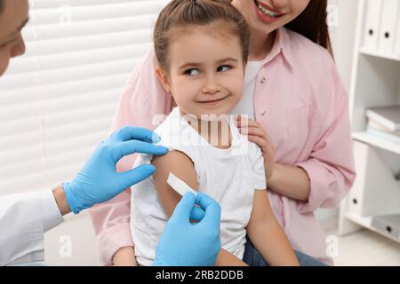 Children's hepatitis vaccination. Mother with her daughter in clinic. Doctor sticking medical plaster on little girl's arm Stock Photo