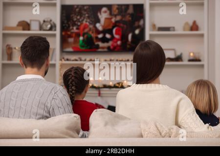 Family watching Christmas movie via TV in cosy room, back view. Winter holidays atmosphere Stock Photo