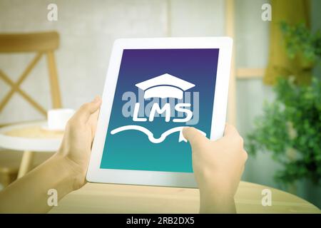 Learning management system. Woman using tablet at table, closeup. Open book and graduate cap icons with abbreviation LMS on screen Stock Photo