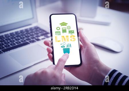 Learning management system. Woman using mobile phone at table, closeup. Different icons and abbreviation LMS on screen Stock Photo