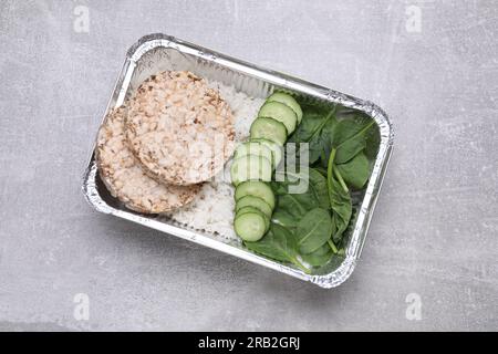 Container with rice, puffed crunchy cakes. fresh spinach and cut cucumbers on light grey table, top view Stock Photo