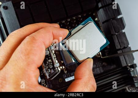 Technician is carefully inserting CPU into motherboard socket during a desktop computer assembly. Stock Photo