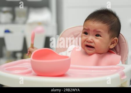 crying infant baby eating food with a spoon at home Stock Photo